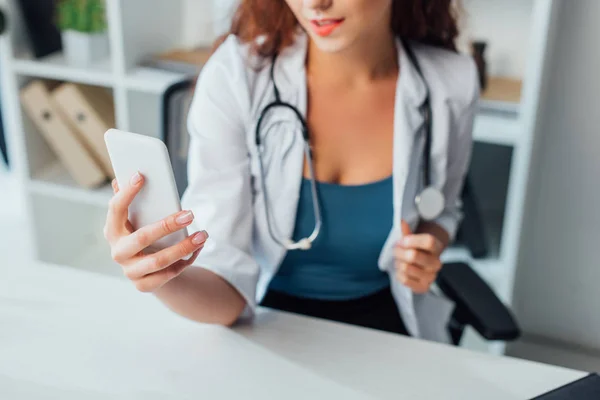 Recortado vista de rizado y sexy enfermera tomando selfie en clínica - foto de stock
