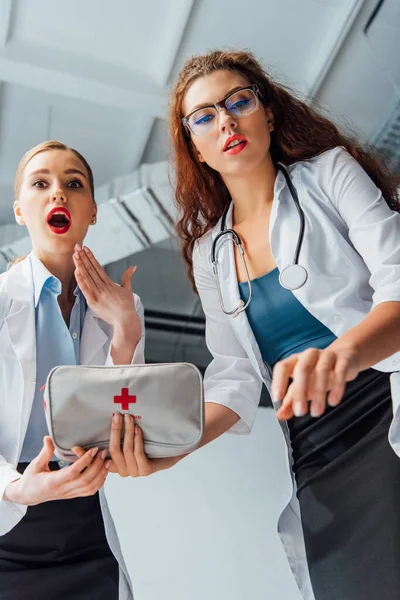 Low angle view of shocked and sexy nurses in white coats with first aid kit — Stock Photo
