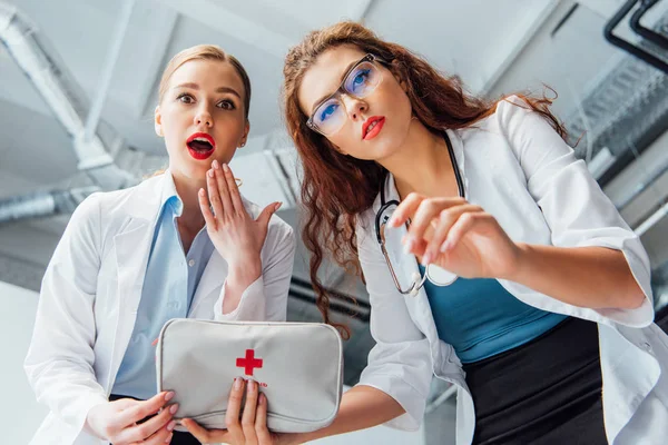 Low angle view of surprised and sexy nurses in white coats with first aid kit — Stock Photo