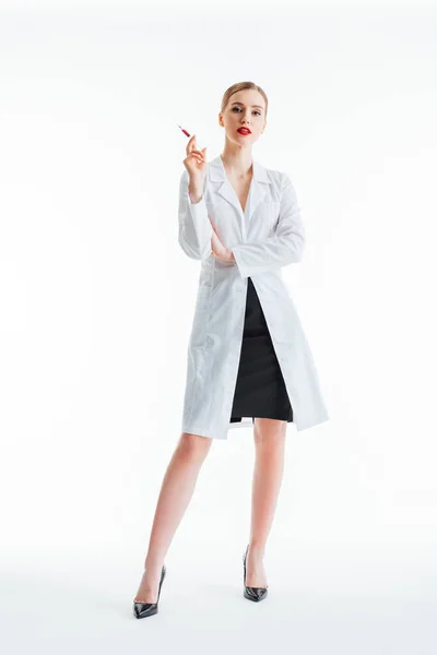 Сексуальна медсестра в білому пальто, що стоїть з шприцом на білому — стокове фото