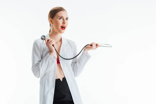 Enfermera sexy excitada en blanco abrigo celebración estetoscopio aislado en blanco - foto de stock