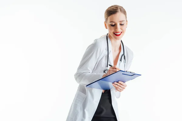 Cheerful and sexy nurse writing prescription while holding clipboard isolated on white — Stock Photo