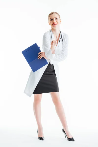 Улыбающаяся сексуальная медсестра, держащая планшет и ручку, стоя на белом — стоковое фото