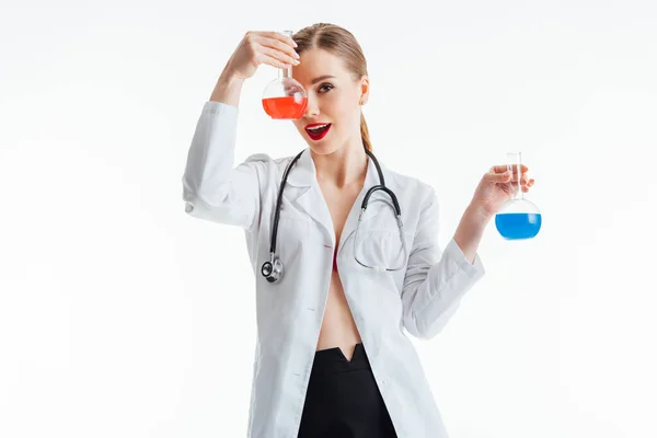 Веселая и сексуальная медсестра, держащая фляжки с красной и синей жидкостью изолированы на белом — стоковое фото