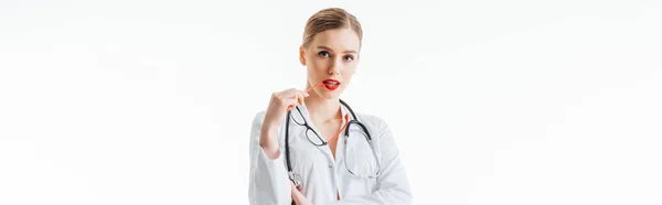 Tiro panorámico de enfermera sexy sosteniendo gafas cerca de labios rojos aislados en blanco - foto de stock