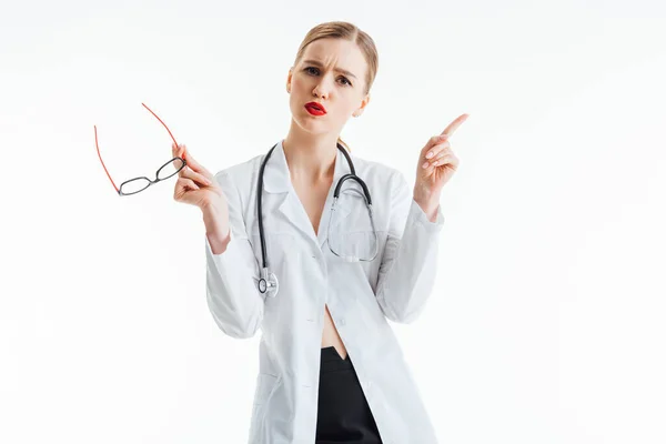 Сексуальна медсестра тримає окуляри і вказує пальцем ізольовано на білому — стокове фото