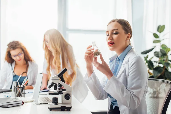 Enfoque selectivo de hermosa y sexy enfermera mirando frasco cerca de las mujeres en batas blancas - foto de stock