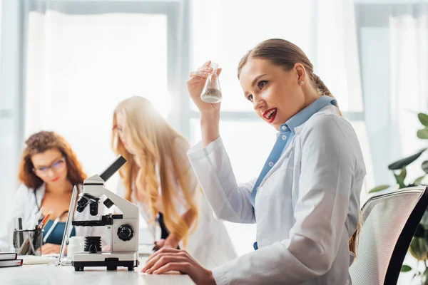 Selective focus of beautiful and sexy nurse holding flask near women in white coats — Stock Photo