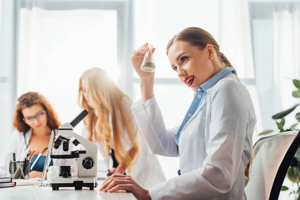 Enfoque selectivo de hermosa y sexy enfermera sosteniendo frasco cerca de las mujeres en batas blancas - foto de stock