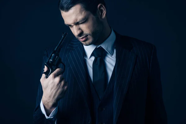 Front view of mafioso looking at revolver in hand on dark background — Stock Photo