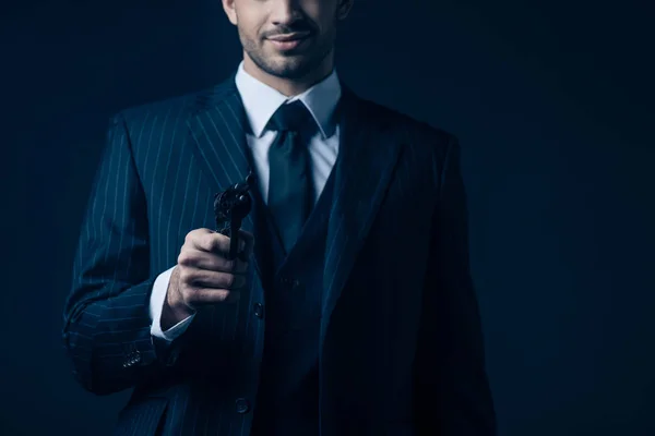 Cropped view of gangster aiming gun and smiling on dark background — Stock Photo