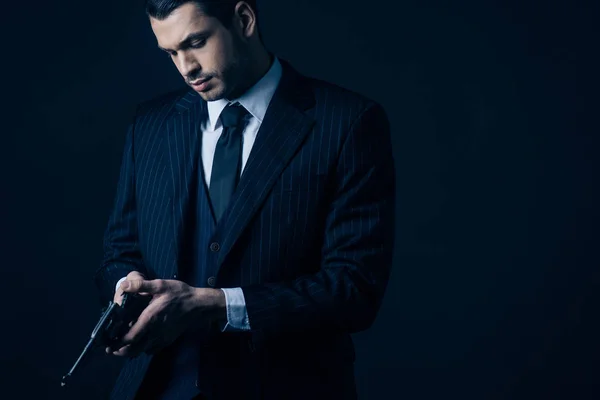 Gangster in elegant suit loading revolver on black background — Stock Photo