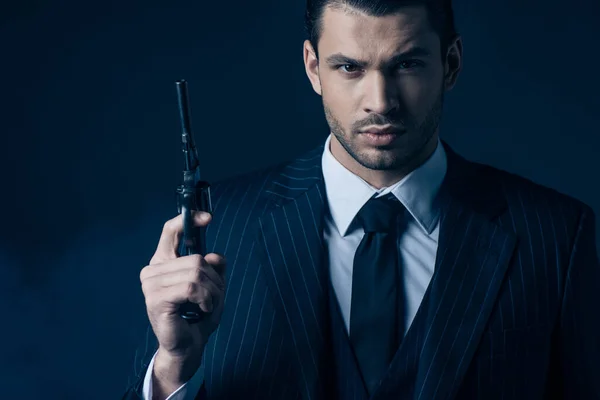 Front view of gangster holding gun and looking at camera on dark blue background — Stock Photo