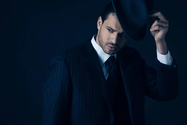 Thoughtful and worried mafioso touching felt hat on dark blue — Stock Photo