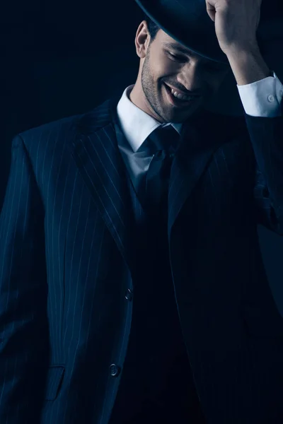 Front view of mafioso holding felt hat and laughing on dark background — Stock Photo