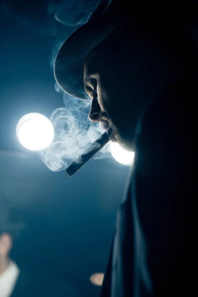 Low angle view of mafioso smoking cigar on dark — Stock Photo