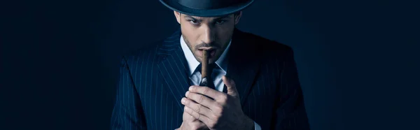 Mafioso lighting cigar and looking at camera on dark, panoramic shot — Stock Photo