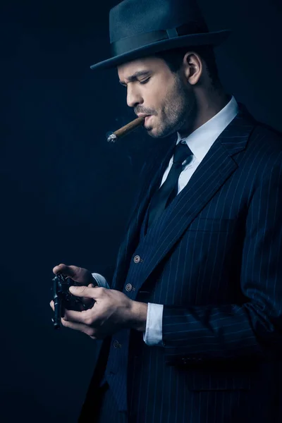 Gangster with cigar in mouth loading revolver on dark blue — Stock Photo