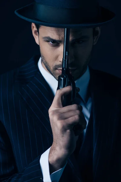 Gángster sosteniendo la pistola delante de la cara en azul oscuro - foto de stock