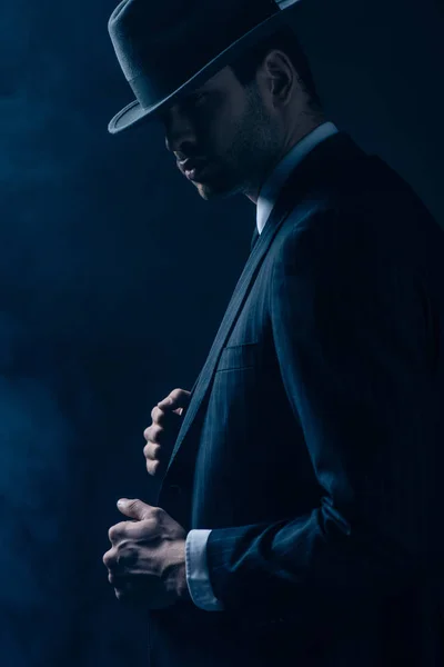 Side view of confident mafioso in black suit and felt hat on dark background — Stock Photo