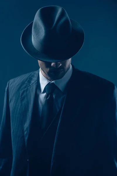 Mafioso con ojos cubiertos con sombrero de fieltro sobre fondo azul oscuro - foto de stock