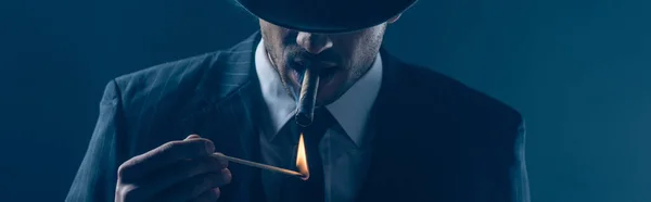 Mafioso lighting cigar with match on dark blue, panoramic shot — Stock Photo