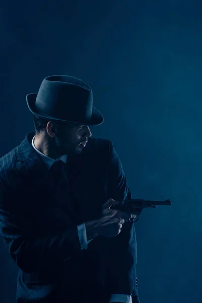 Gángster sosteniendo pistola y apuntando sobre fondo azul oscuro - foto de stock