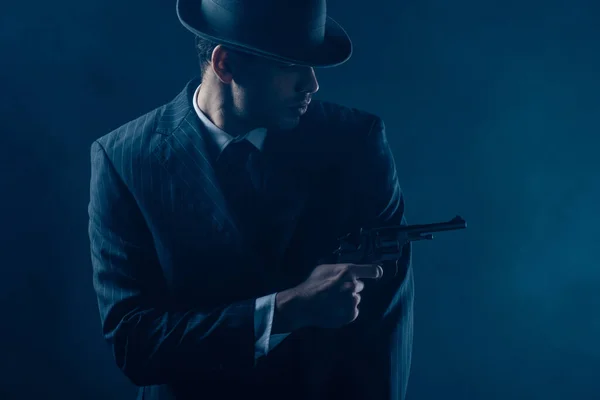 Gangster pointing revolver aside on dark blue background — Stock Photo