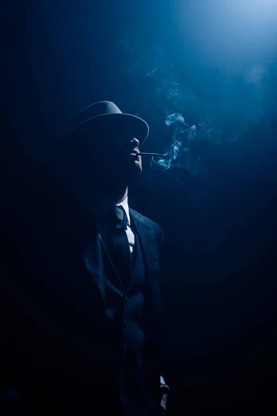 Silhouette of mafioso smoking cigarette on dark blue background — Stock Photo