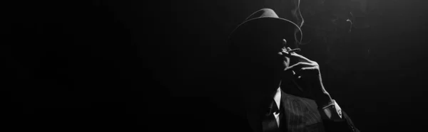 Monochrome image of mafioso silhouette smoking on black background, panoramic shot — Stock Photo