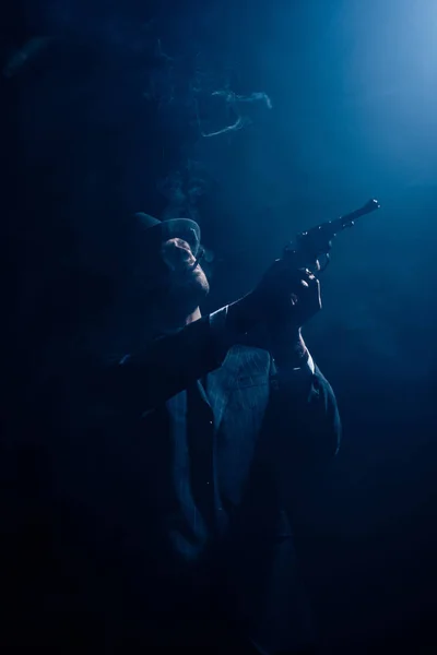 Silueta de gángster apuntando arma y humeante sobre fondo azul oscuro - foto de stock