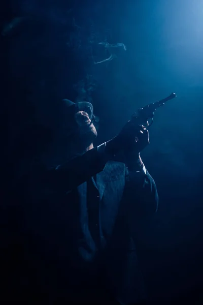 Silhouette de gangster visant pistolet et fumer sur fond bleu foncé — Photo de stock