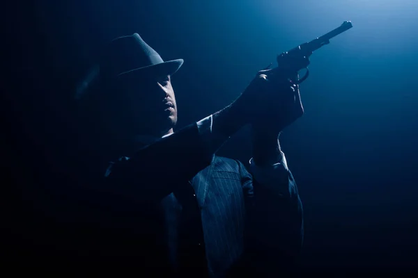 Gangster com as mãos estendidas apontando revólver no fundo escuro — Fotografia de Stock