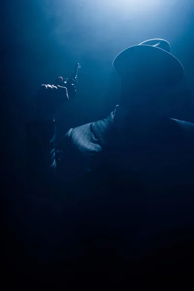 Силуэт гангстера в костюме и войлочной шляпе с пистолетом на темном фоне — стоковое фото