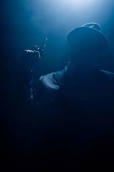 Silhouette of gangster in suit and felt hat with gun on dark background — Stock Photo