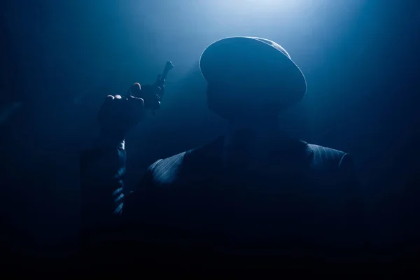 Silhouette de gangster en costume et chapeau en feutre avec revolver sur fond sombre — Photo de stock