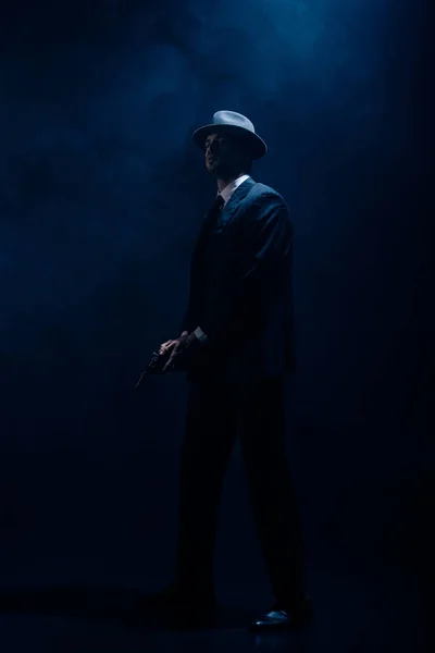 Dangerous gangster with weapon in clenched hands on dark blue background — Stock Photo