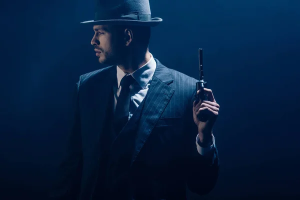 Gangster raising revolver and looking away on dark background — Stock Photo