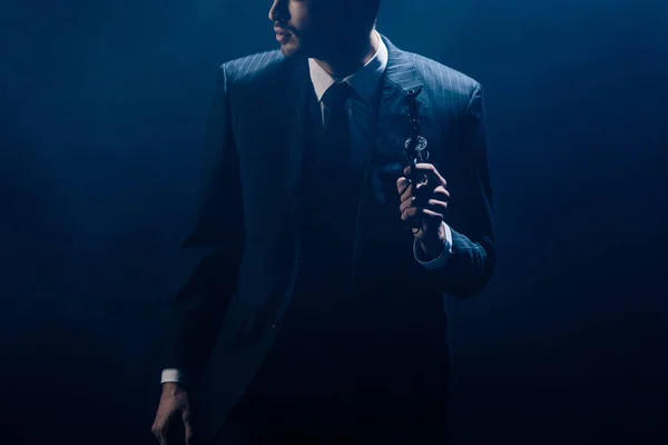 Ausgeschnittener Blick auf Gangster, der Revolver hebt und auf dunklem Hintergrund wegschaut — Stockfoto