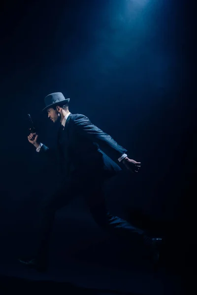 Gangster levantando a mão com arma e correndo em fundo azul escuro — Fotografia de Stock