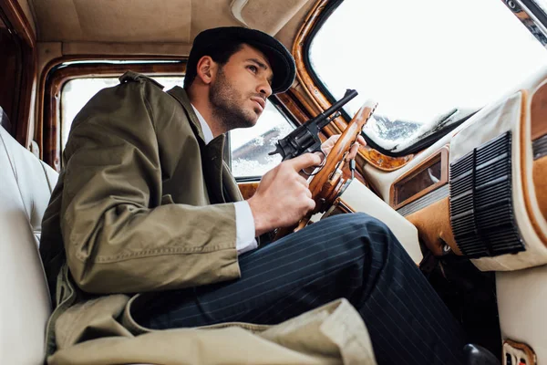 Low angle view of mafioso holding gun and driving car — Stock Photo
