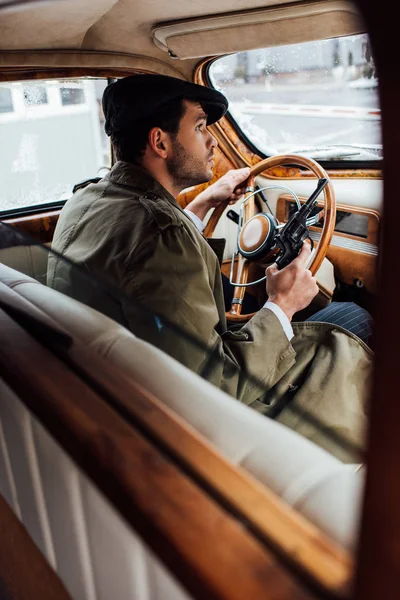 Selective focus of gangster holding gun and steering wheel in car — Stock Photo