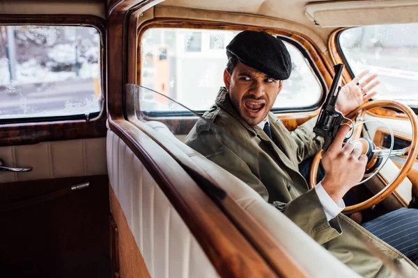 Selective focus of irritated gangster with revolver screaming in car — Stock Photo