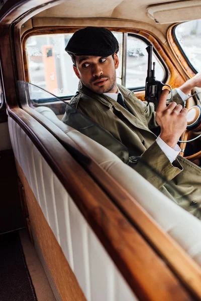 Selective focus of gangster with gun looking back in car — Stock Photo