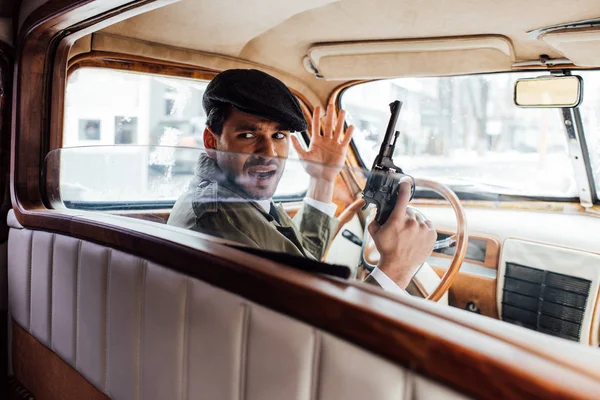 Selective focus of irritated gangster with gun looking back in car — Stock Photo