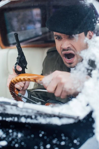 Selective focus of dangerous angry gangster with gun shouting and driving car — Stock Photo