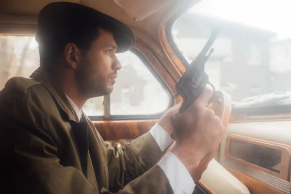 Profile of mafioso in flat cap and coat with gun driving car — Stock Photo