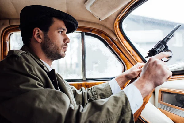 Selective focus of gangster in flat cap and coat with gun driving car — Stock Photo