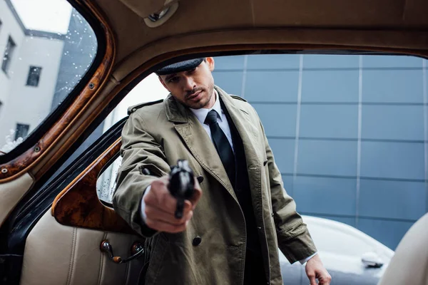 Selective focus of mafioso aiming gun with outstretched hand into retro car — Stock Photo