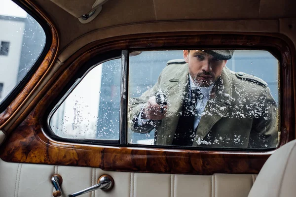 Peligroso mafioso apuntando arma y mirando en coche retro - foto de stock